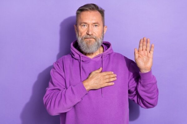 Man in purple hood with hand on heart and hand raised in swearing in pose